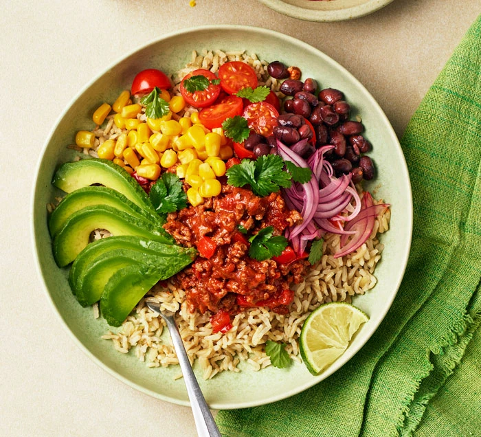 Vibrant beef taco bowl with rice, black beans, corn, cherry tomatoes, pickled red onion, avocado, and lime