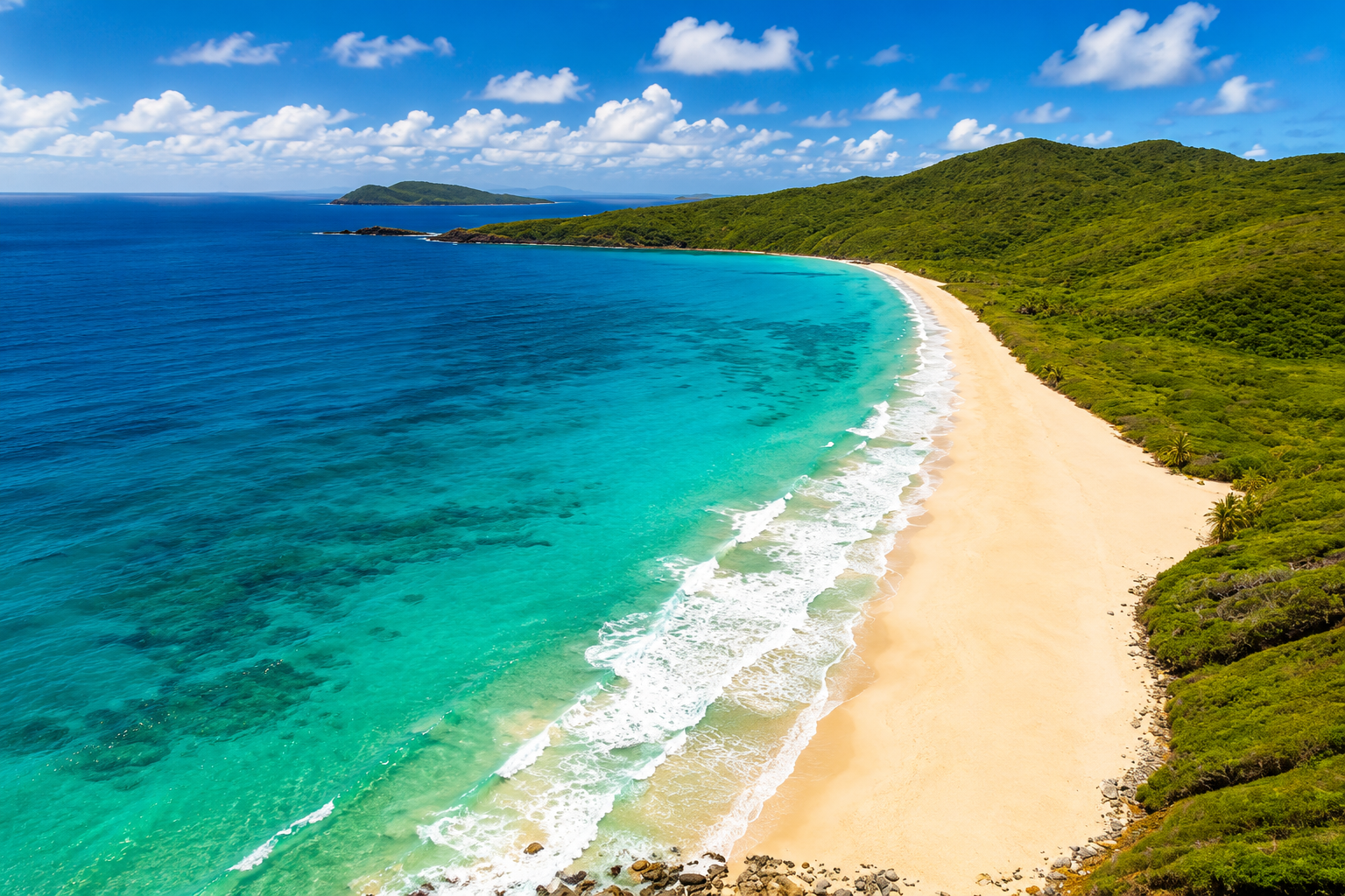 An aerial view of Resaca Beach — a long curve of golden sand bordered by turquoise water and green hillsides
