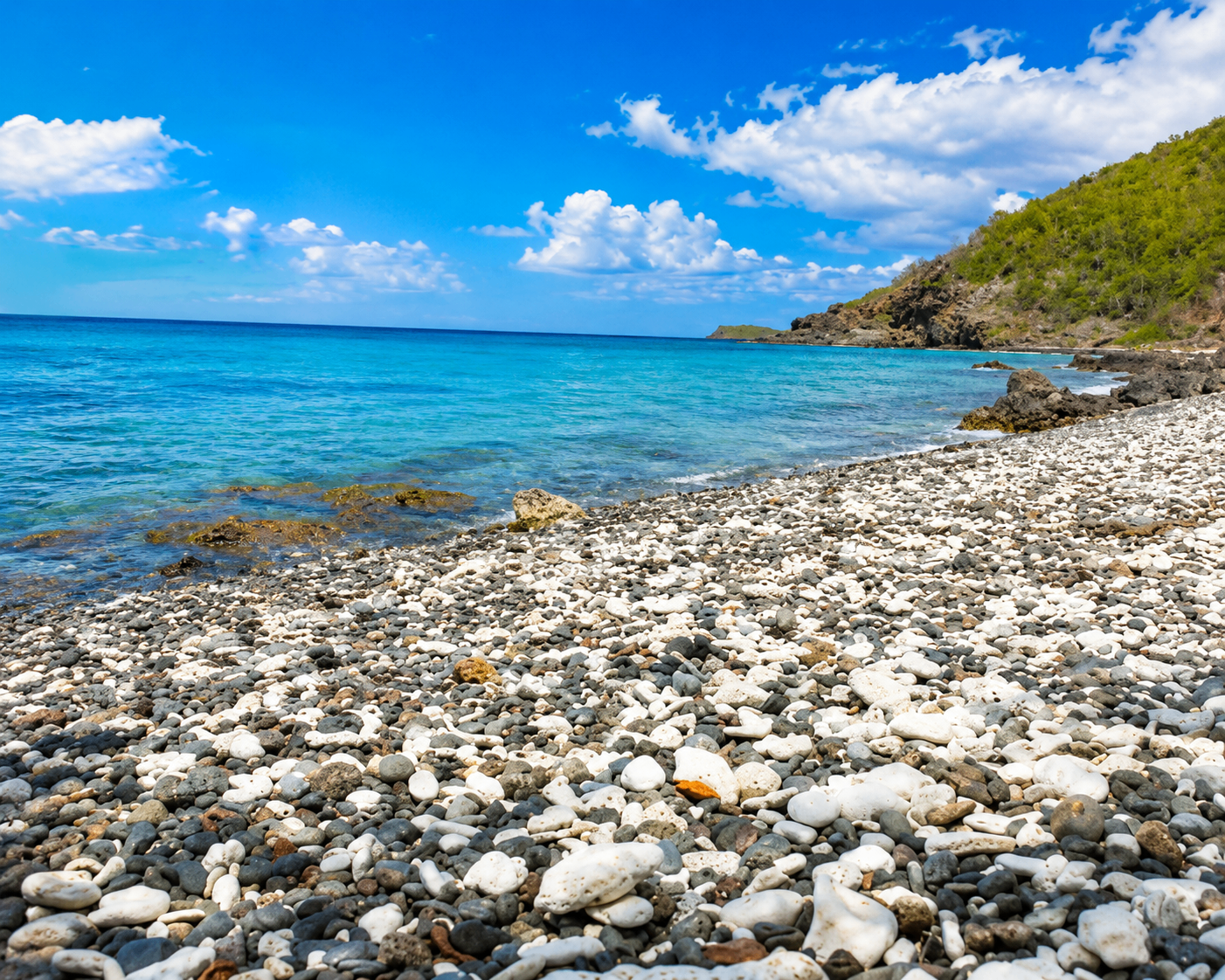 Pebble and coral shoreline at Punta Soldado with clear turquoise water and a green hillside