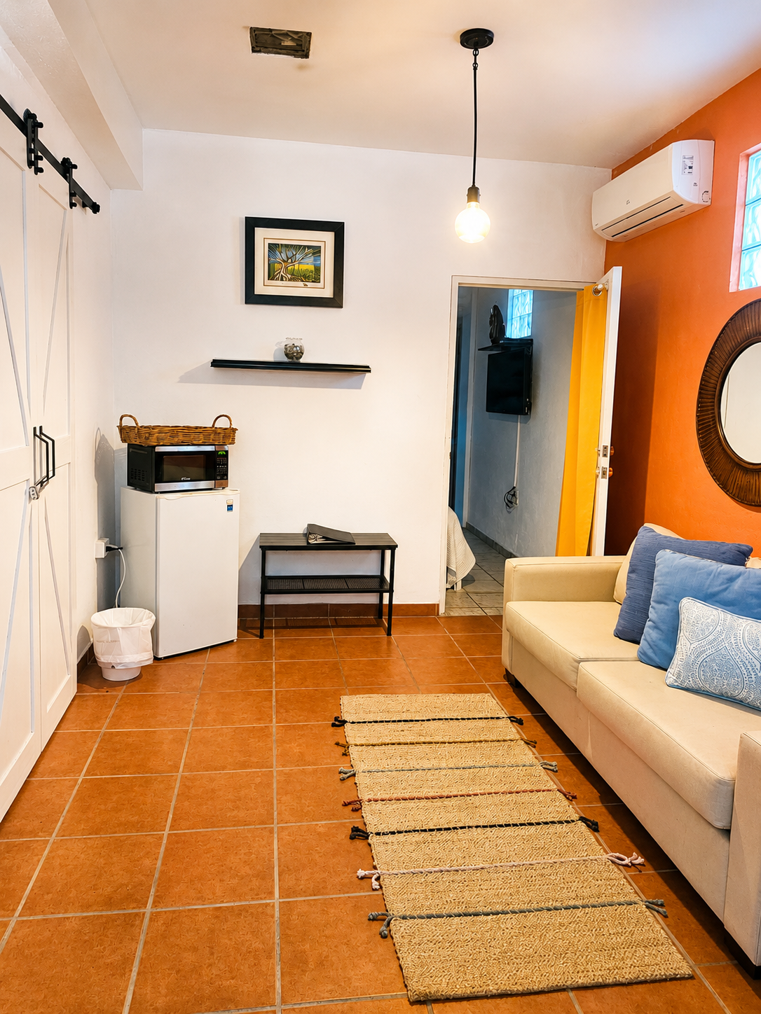 Interior of Sirena Apartment — bright street-level living area with sofa, mini fridge, microwave, and warm accent wall