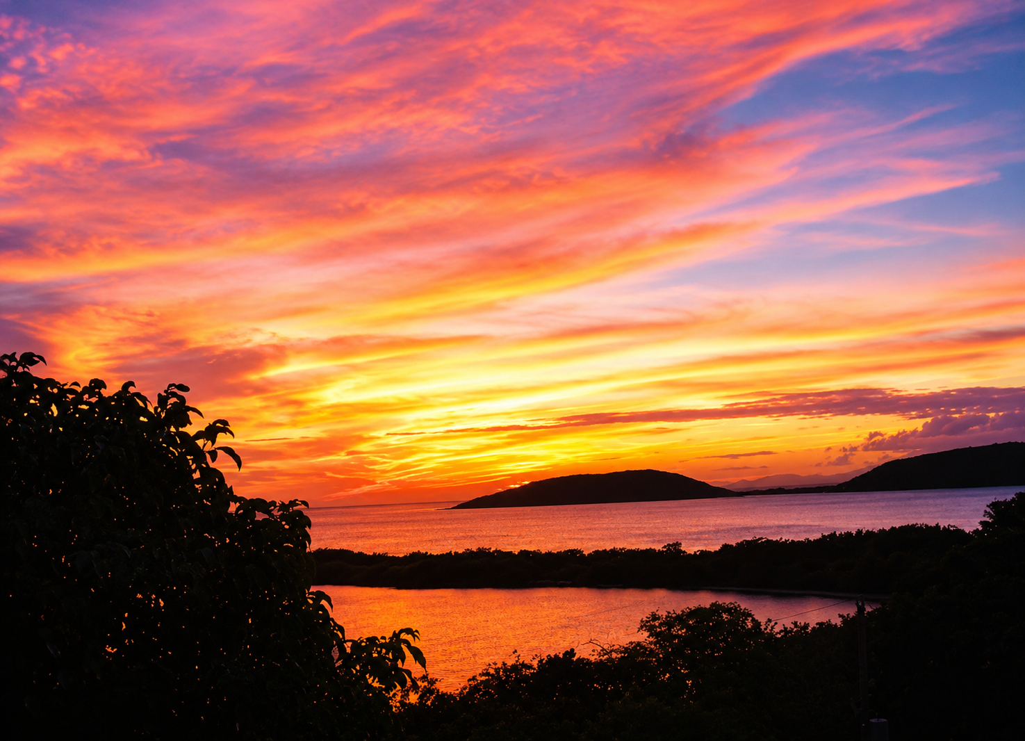 A brilliant orange and pink sunset over the water at Melones, with silhouetted islands on the horizon